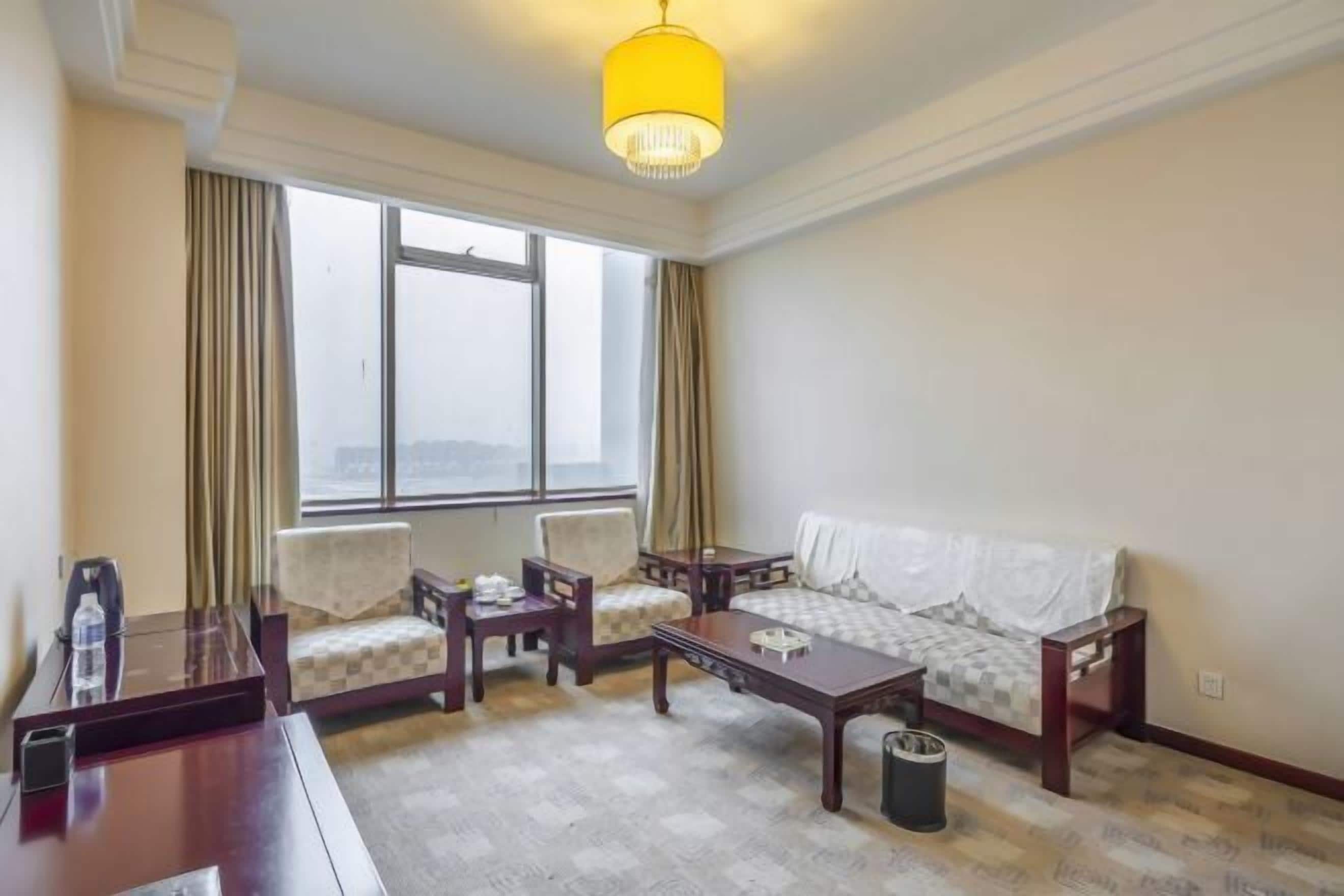 A hotel room with a large window, a sofa, two armchairs, a coffee table, and a desk with a chair.