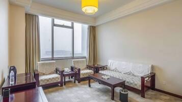 A hotel room with a large window, a sofa, two armchairs, a coffee table, and a desk with a chair.