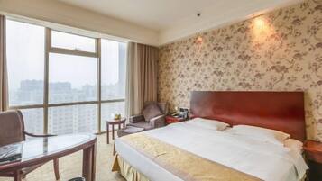 A hotel room with a large bed, a desk, a chair, a small table, and a window with a view of buildings.