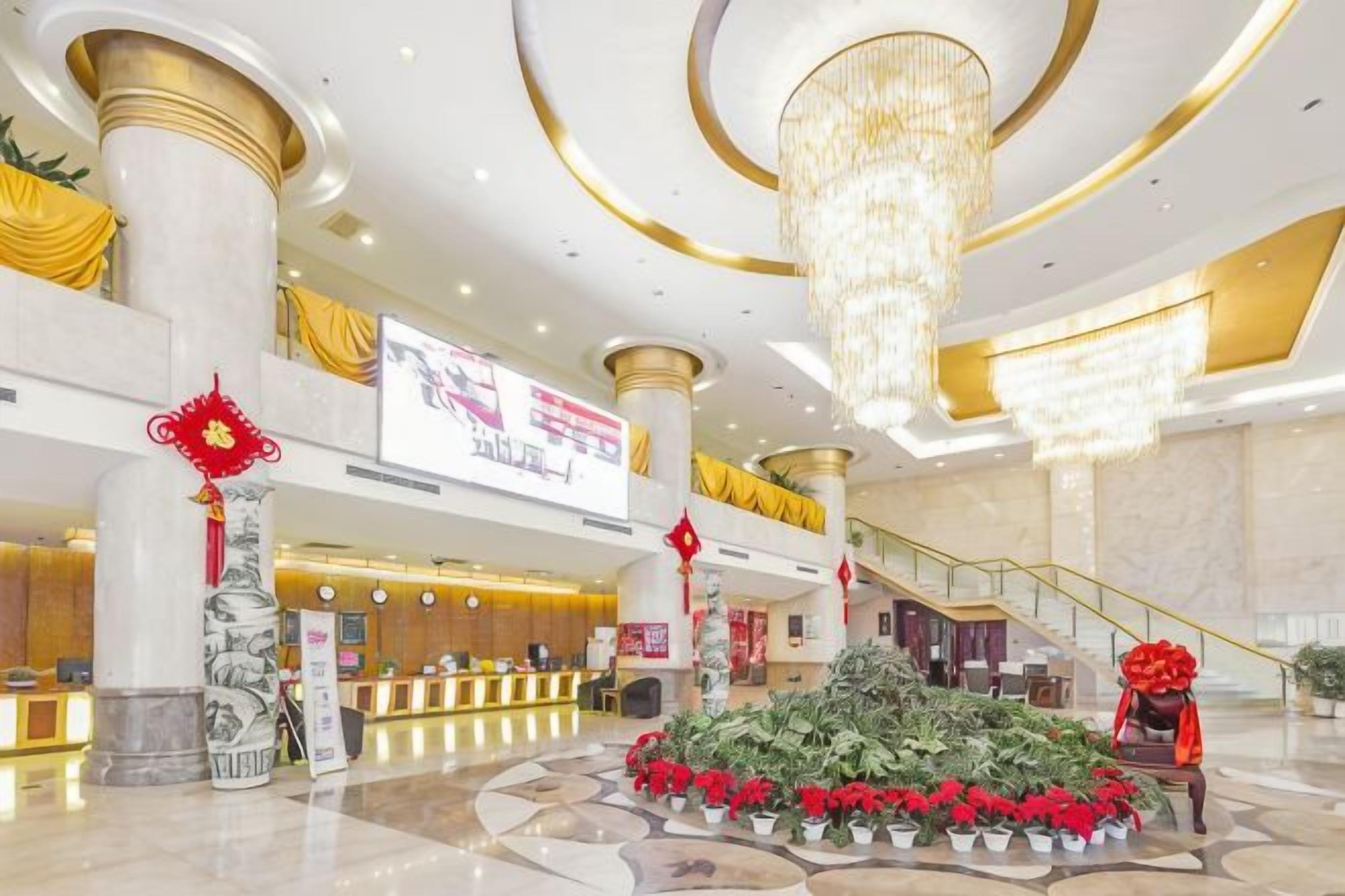 Vestíbulo de hotel con mostrador de recepción, una escalera y una decoración floral.