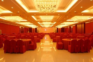 Une salle de banquet avec des rangées de tables rondes et de chaises, une allée centrale et un lustre.
