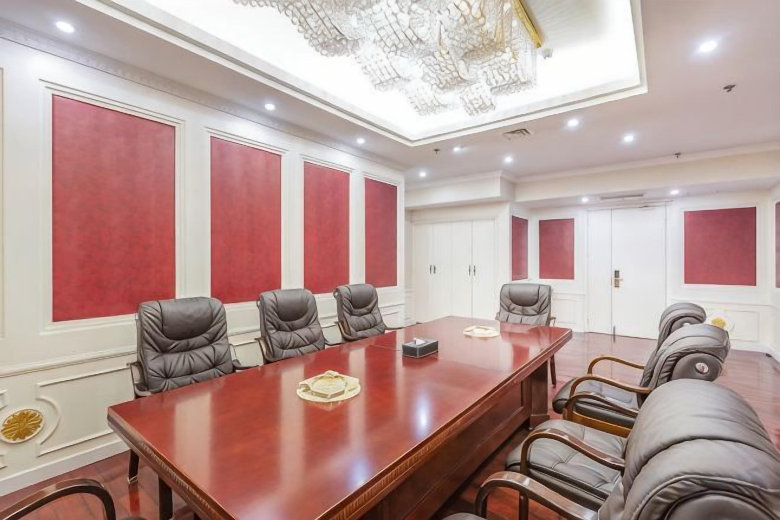 A conference room with a long table and multiple chairs, a chandelier, and red accent walls.