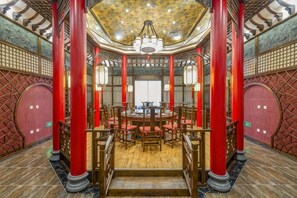 A traditional interior with a central round table surrounded by chairs, red pillars, and a patterned ceiling. - Mei Di Ya Zhong Hua Hotel (Zhuolu)