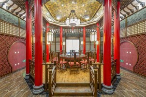 A traditional interior with a central round table surrounded by chairs, red pillars, and a patterned ceiling.