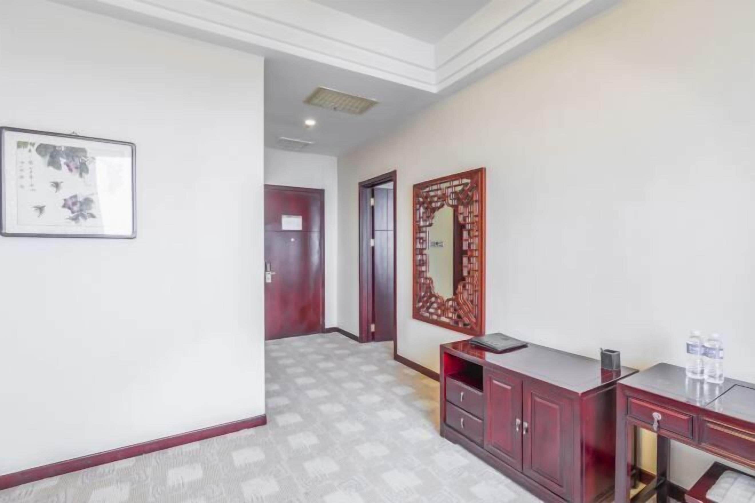 A hallway with a patterned floor, a wooden cabinet with drawers, a framed artwork on the wall, and a door in the background.