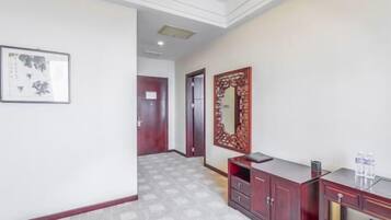 A hallway with a patterned floor, a wooden cabinet with drawers, a framed artwork on the wall, and a door in the background.