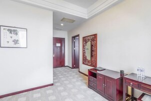 A hallway with a patterned floor, a wooden cabinet with drawers, a framed artwork on the wall, and a door in the background.
