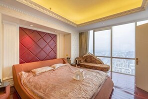 Un grand lit avec une tête de lit rouge, un canapé et une vue sur le paysage urbain à travers de grandes fenêtres.