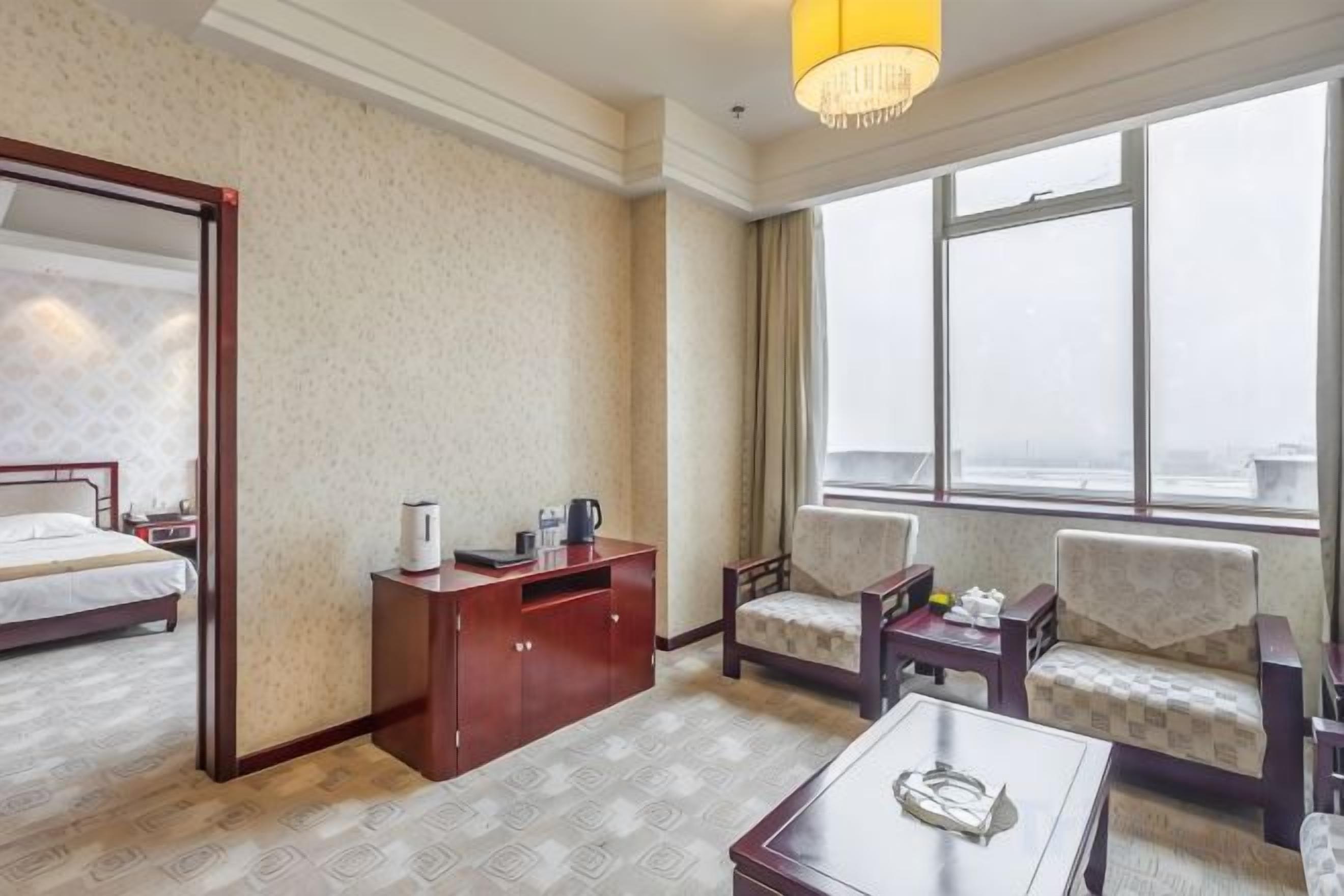 A hotel room with a bed, a desk, two chairs, a coffee table, and a large window.
