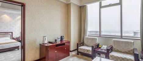 A hotel room with a bed, a desk, two chairs, a coffee table, and a large window.
