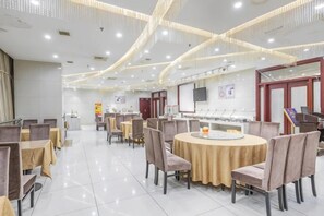 Un comedor amplio con mesas y sillas redondas, piso de baldosas blancas y un diseño de techo moderno con iluminación empotrada.