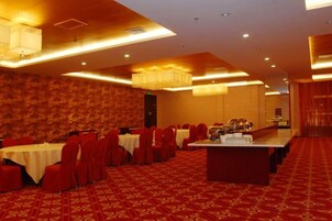 Un salón de banquetes con mesas dispuestas en filas, una zona de bar central y una alfombra estampada.