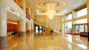 A spacious lobby with a polished marble floor, a grand chandelier, and a staircase leading to upper levels.