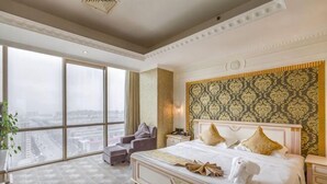 A spacious hotel room with a large bed, a chair, a nightstand, and a view of the city through large windows.
