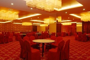 Un salón de banquetes con mesas redondas y sillas rojas, suelo alfombrado y candelabros.