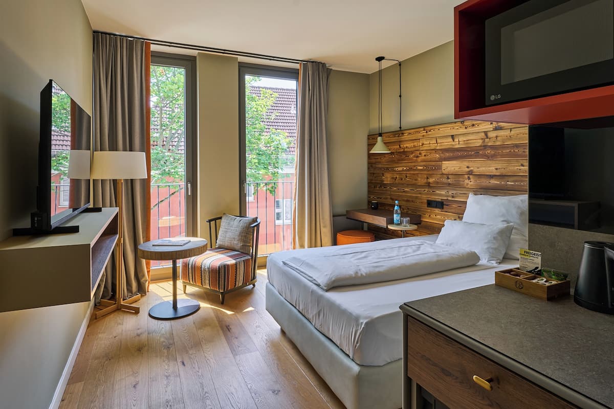 A hotel room with a bed, a desk, a chair, a TV, and a window with curtains.