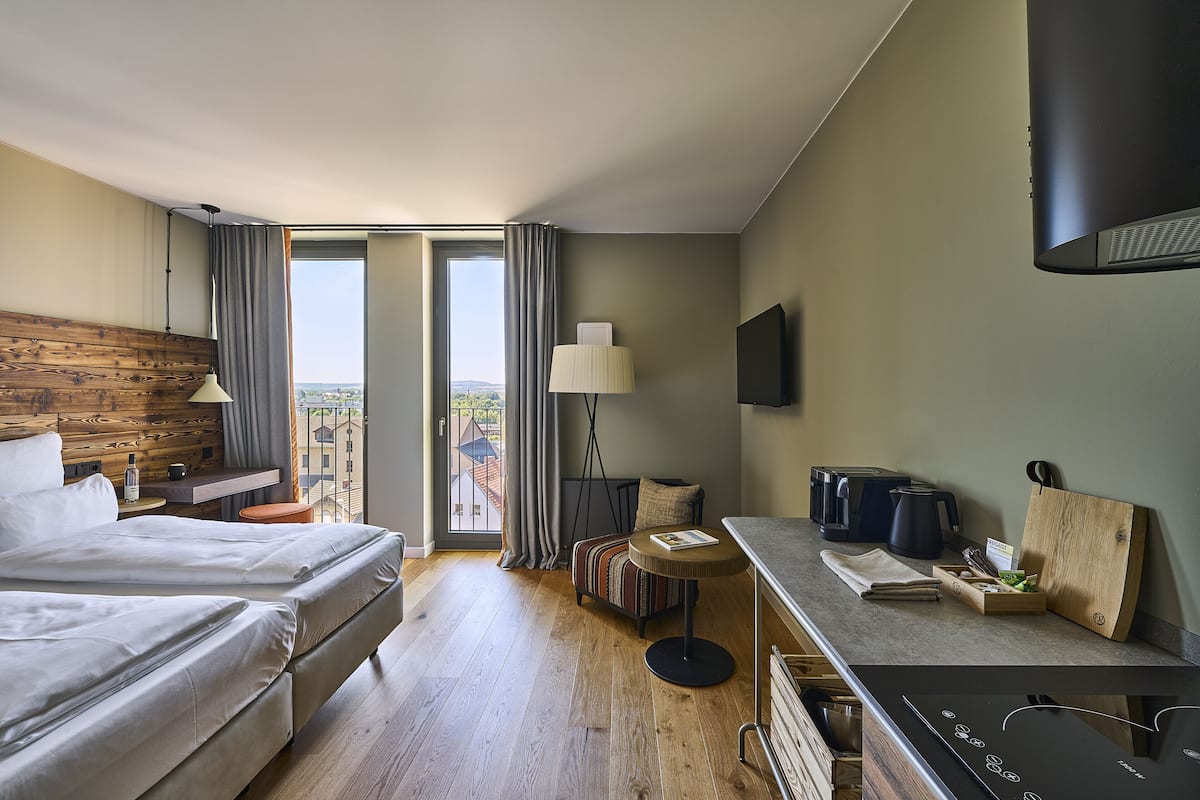 A hotel room with two beds, a dining area, a view of the city, and modern amenities.