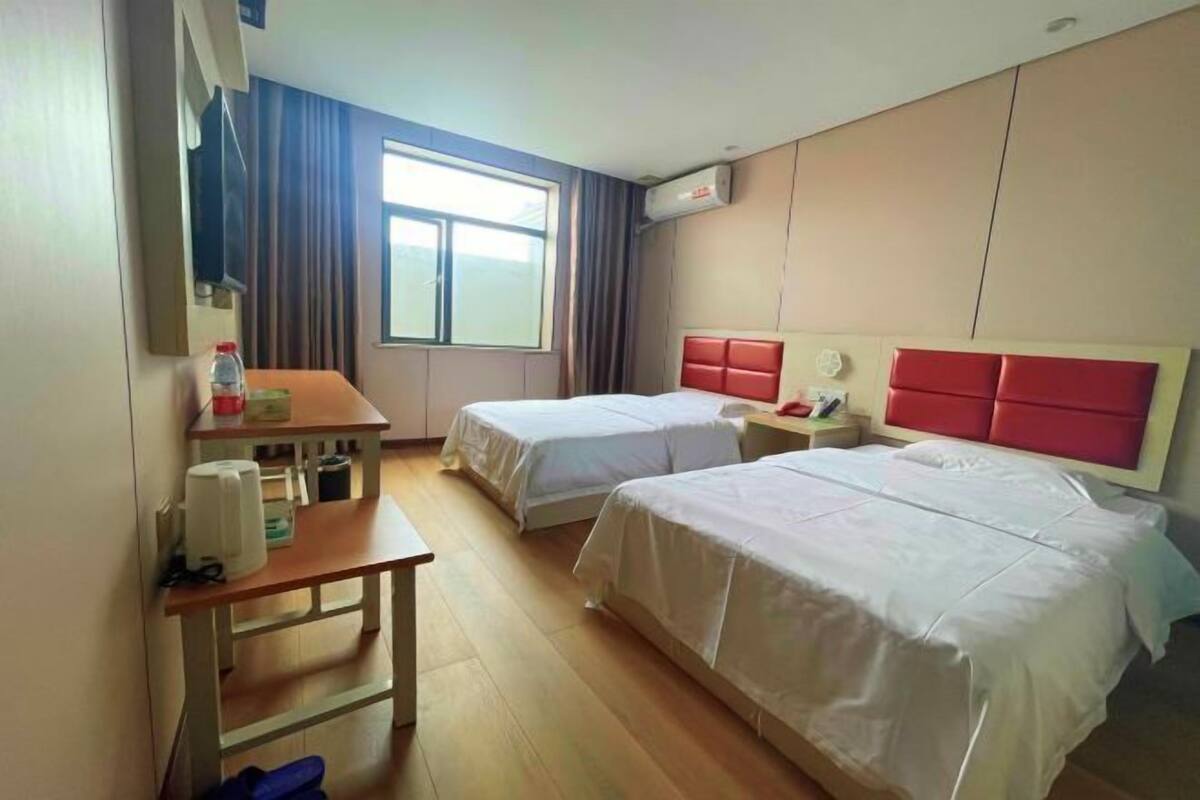 Habitación de hotel con dos camas, un escritorio, una silla, una ventana y un equipo de aire acondicionado.