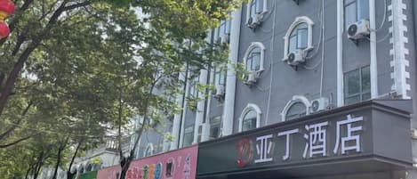 A hotel with a signboard, multiple windows, and a tree in the foreground.