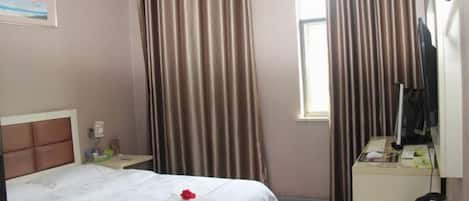 A hotel room with a bed, a desk, a chair, a window, curtains, and a television.