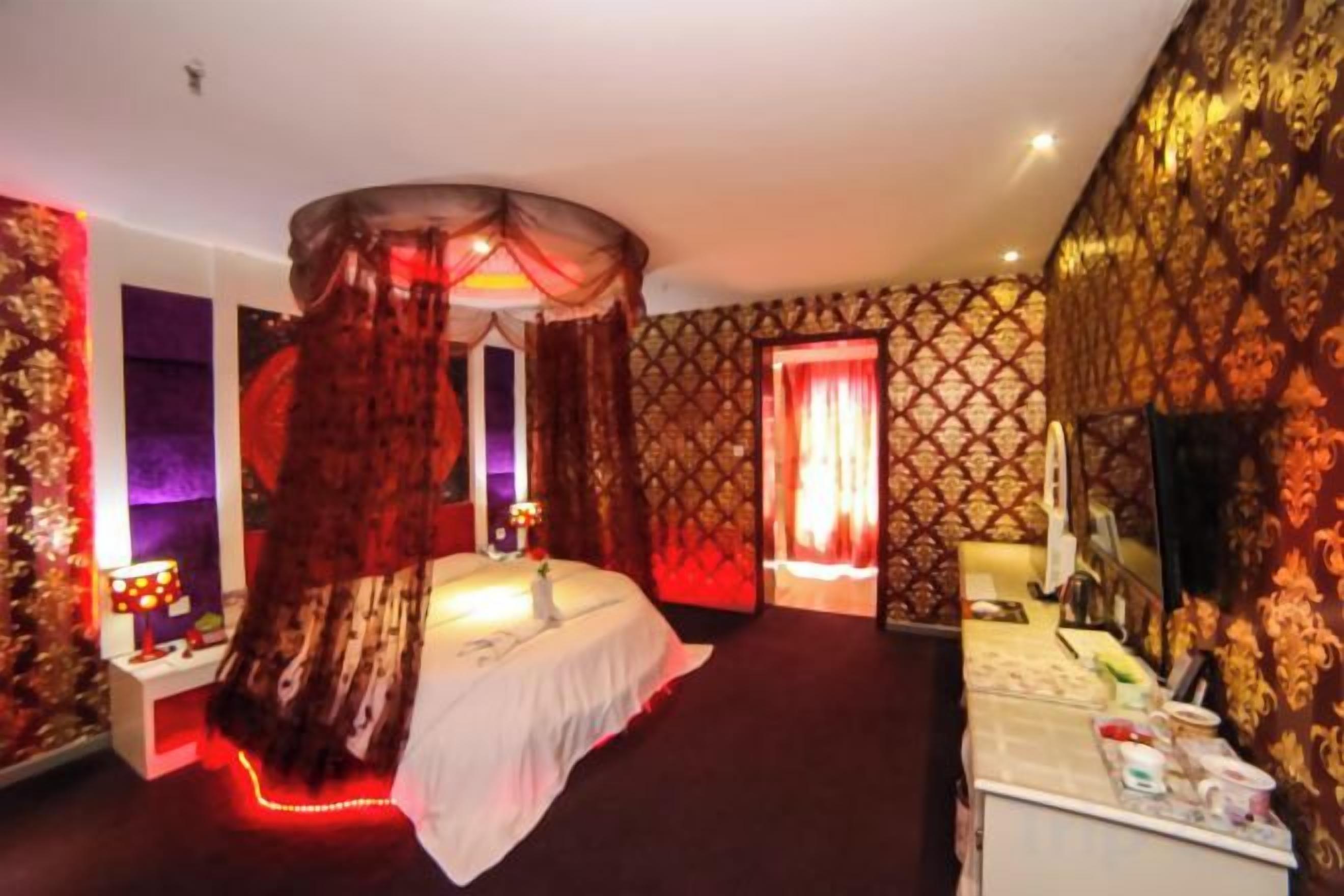 Habitación de hotel con cama con dosel, tocador con espejo y pared iluminada en rojo.