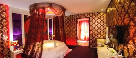 Habitación de hotel con cama con dosel, tocador con espejo y pared iluminada en rojo.