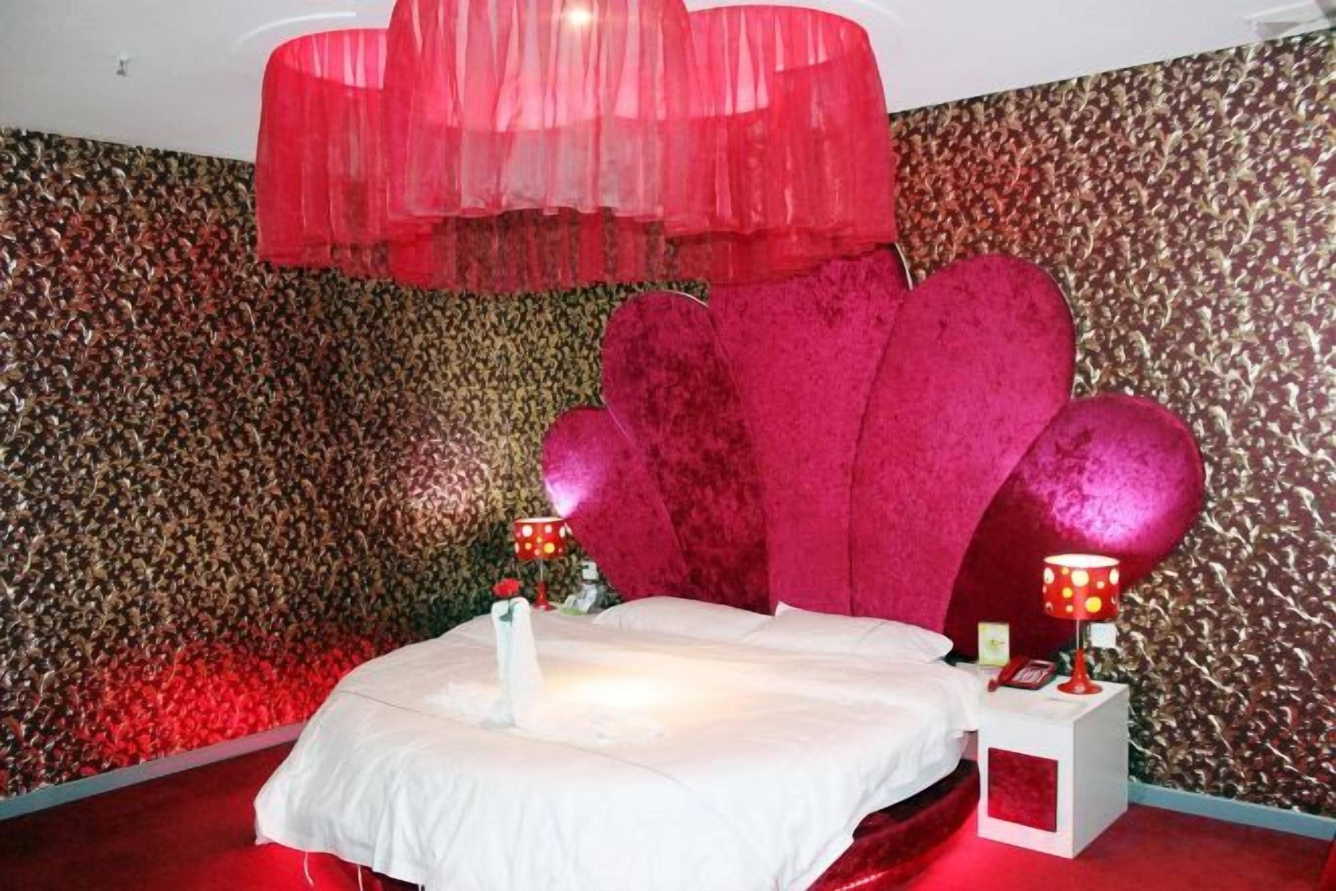 Una cama con una colcha blanca, un dosel rojo y un cabecero con forma de corazón.