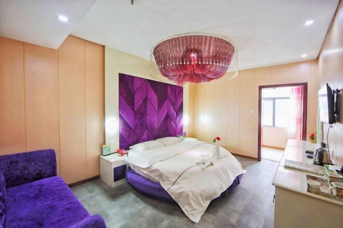 Una habitación de hotel moderna con una cama grande, un sofá púrpura, un panel decorativo en la pared y un candelabro.