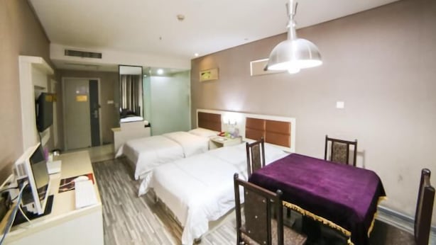 Una camera d'albergo con due letti, una scrivania con un computer, una sedia e una coperta viola.