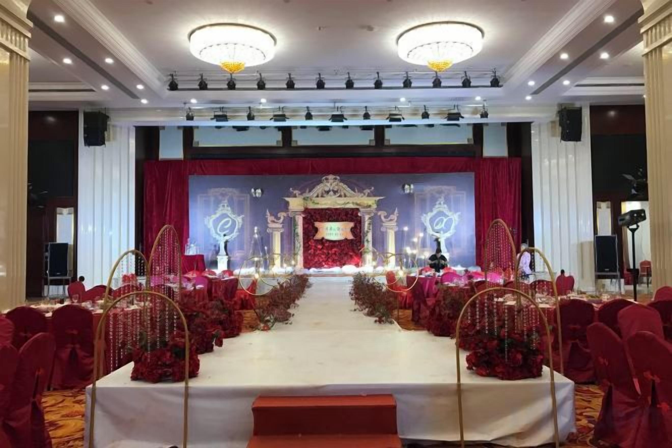 A banquet hall with a stage, rows of tables, and red chairs.