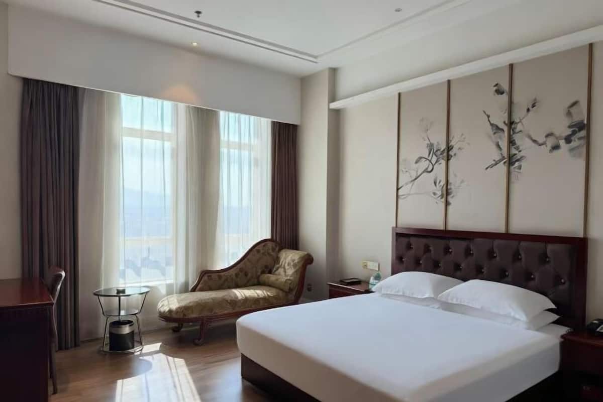 A hotel room with a large bed, a chair, a small table, and a decorative wall piece.