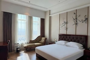 A hotel room with a large bed, a chair, a small table, and a decorative wall piece.