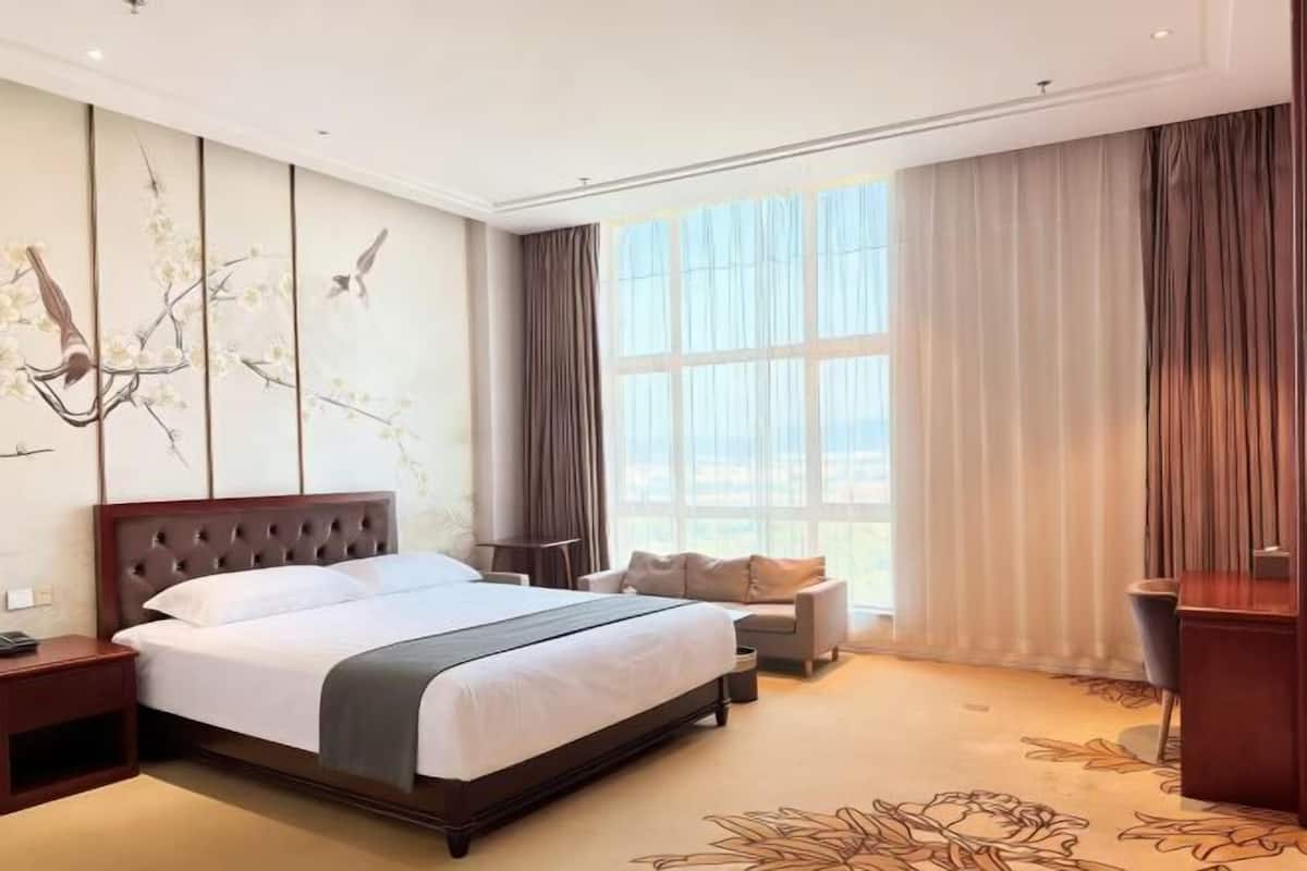 A hotel room with a large bed, a desk, a chair, and a view of the outdoors through a window.