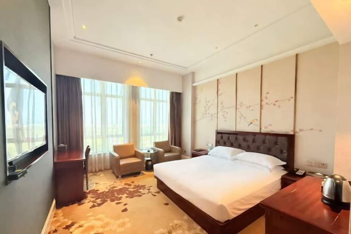 A hotel room with a large bed, a desk, two chairs, a small table, and a decorative wall panel.