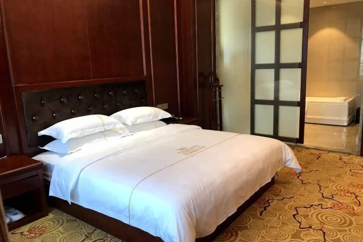 A hotel room with a large bed, wooden headboard, and a patterned carpet.