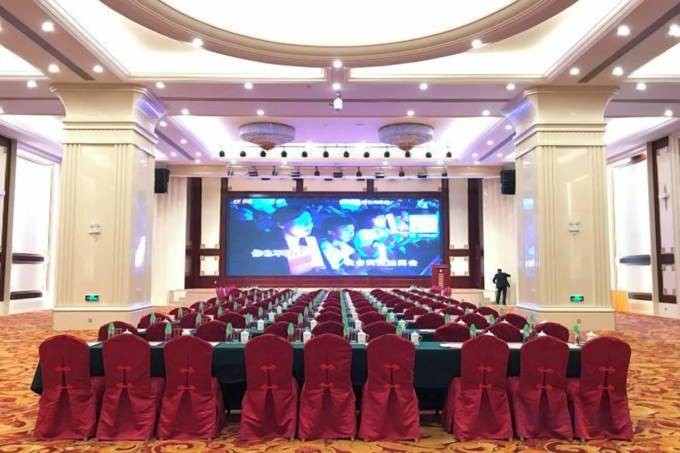 A conference room with rows of tables and chairs, a large screen, and a stage.