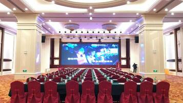 A conference room with rows of tables and chairs, a large screen, and a stage.