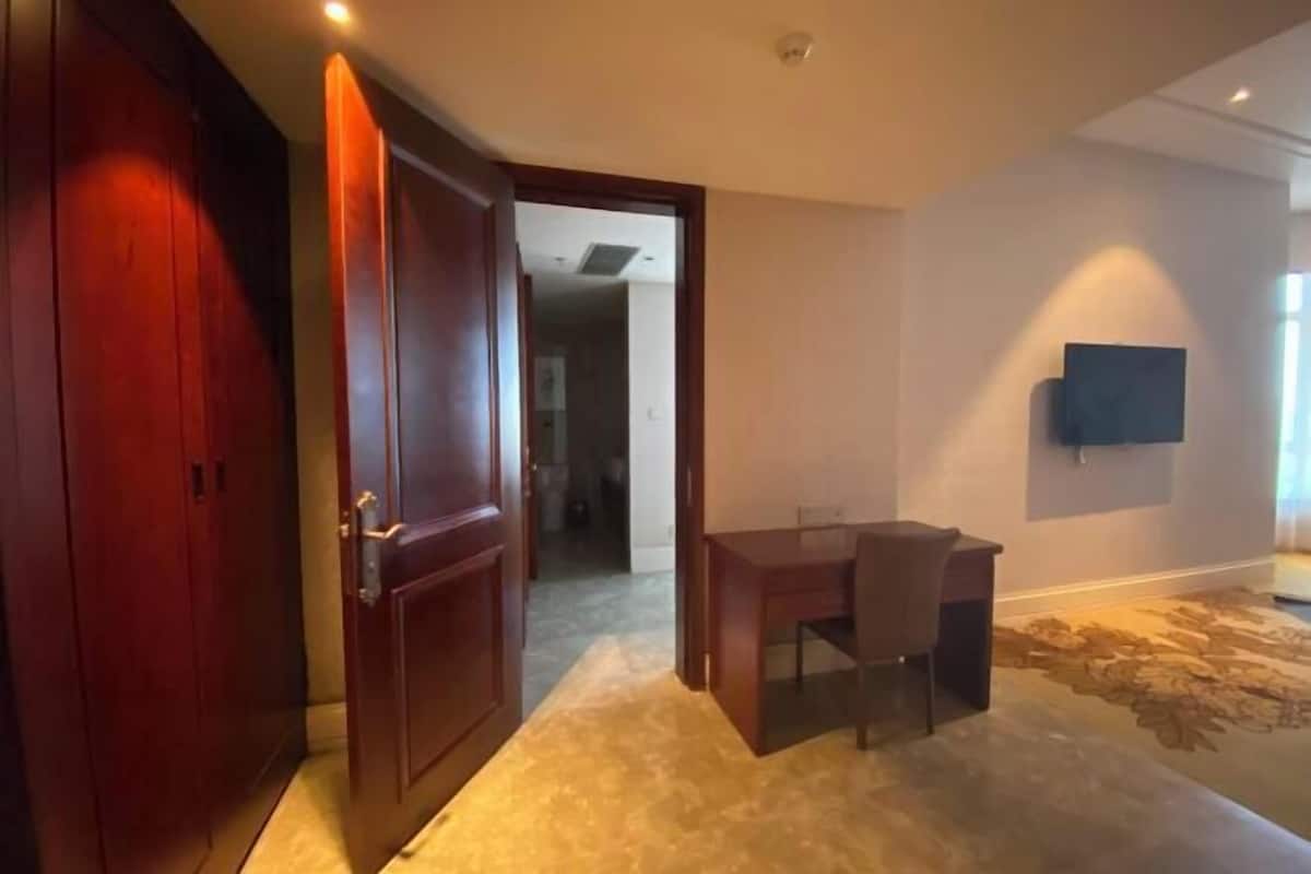 A room with a wooden door, a dining table with chairs, a patterned carpet, and a mounted flat-screen TV on the wall.