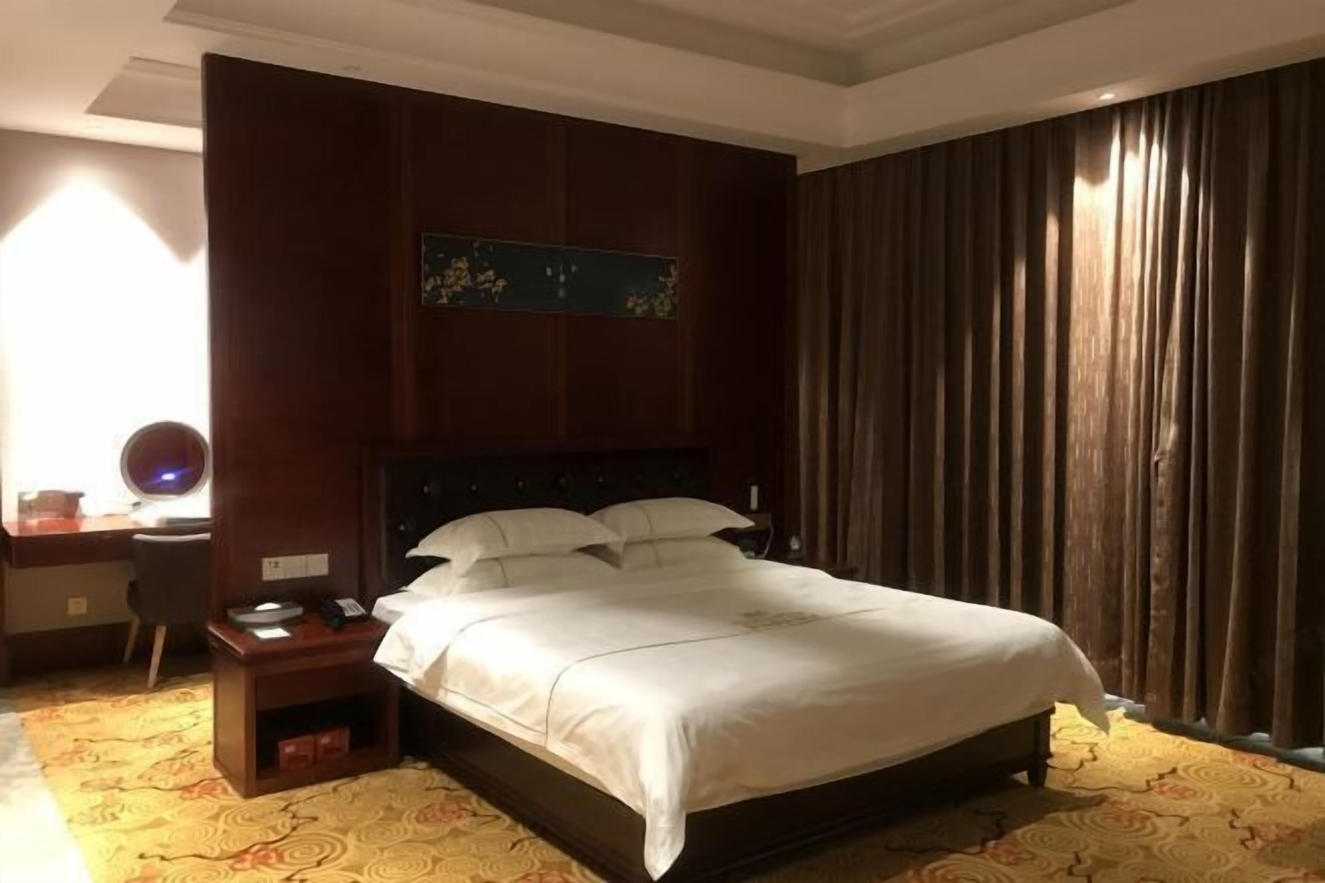 A hotel room with a large bed, a desk with a chair, a nightstand, and a wall-mounted artwork.
