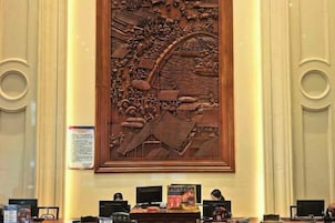 Un mostrador de recepción con múltiples monitores de ordenador, un panel decorativo de madera encima y un cartel informativo enmarcado en la pared.