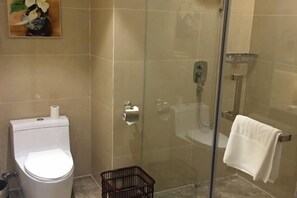 Un baño con inodoro, cabina de ducha de vidrio y toallero.