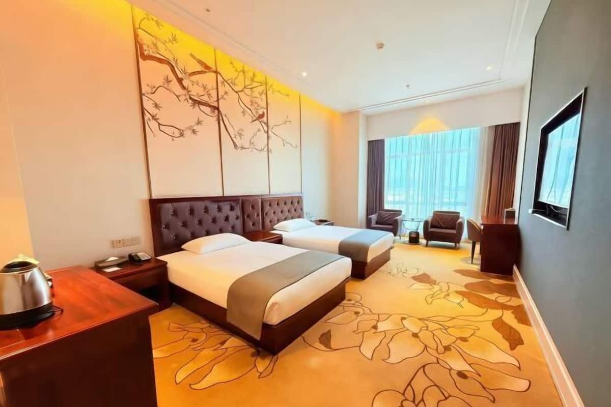 A hotel room with two beds, a large window with curtains, a flat-screen TV, and a decorative wall piece.