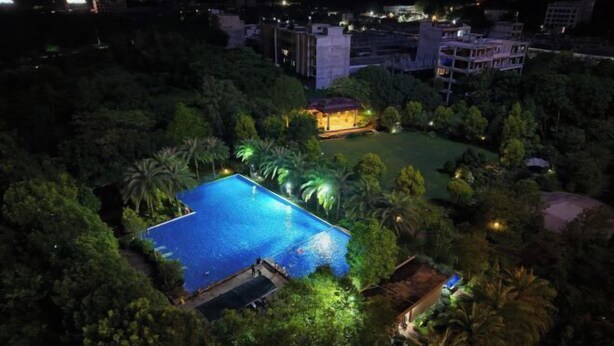 Ein großer, rechteckiger Swimmingpool, umgeben von üppiger Vegetation, mit einem gut beleuchteten Gebäude im Hintergrund.