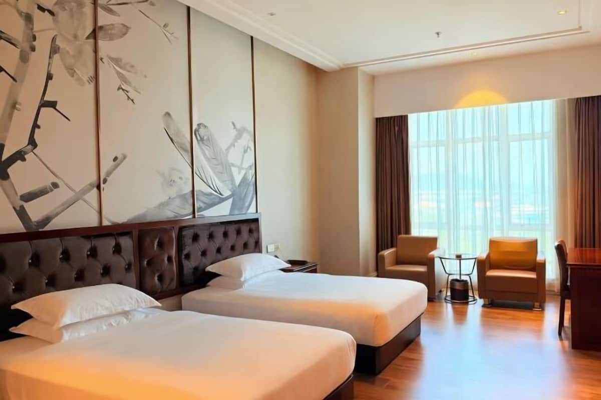 A hotel room with two beds, a large window with curtains, a seating area with chairs, and a wall with a large abstract painting.