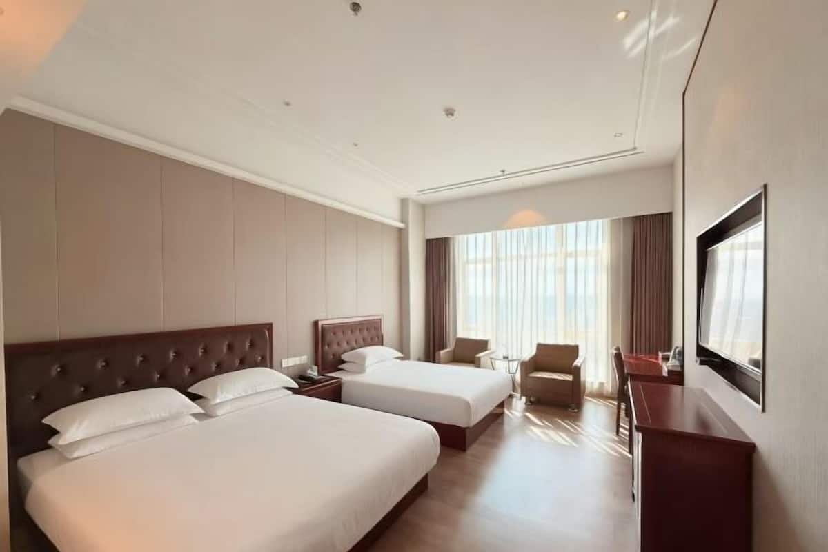 A hotel room with two beds, a TV, a desk, and a chair.