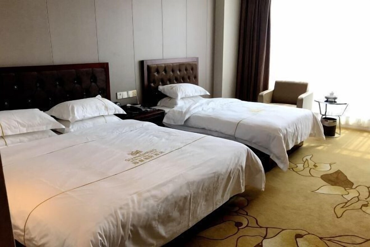 Una habitación de hotel con dos camas, una mesita de noche, una silla y una lámpara.