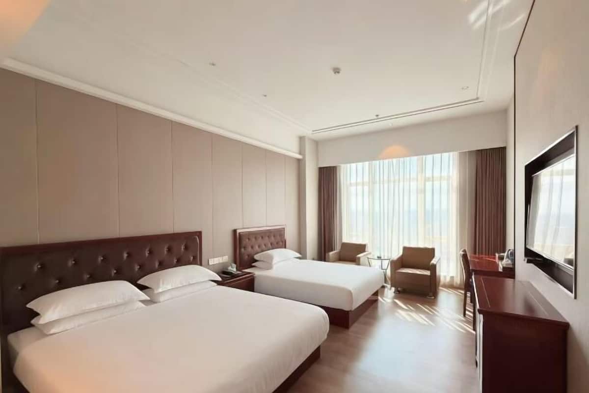 A hotel room with two beds, a desk, a chair, and a large window.