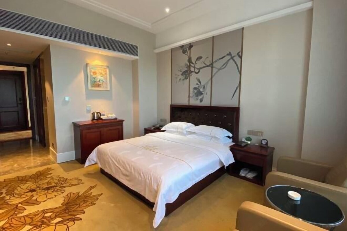 Habitación de hotel con una cama grande, una mesita de noche, una mesilla auxiliar, una pequeña mesa redonda y una silla.