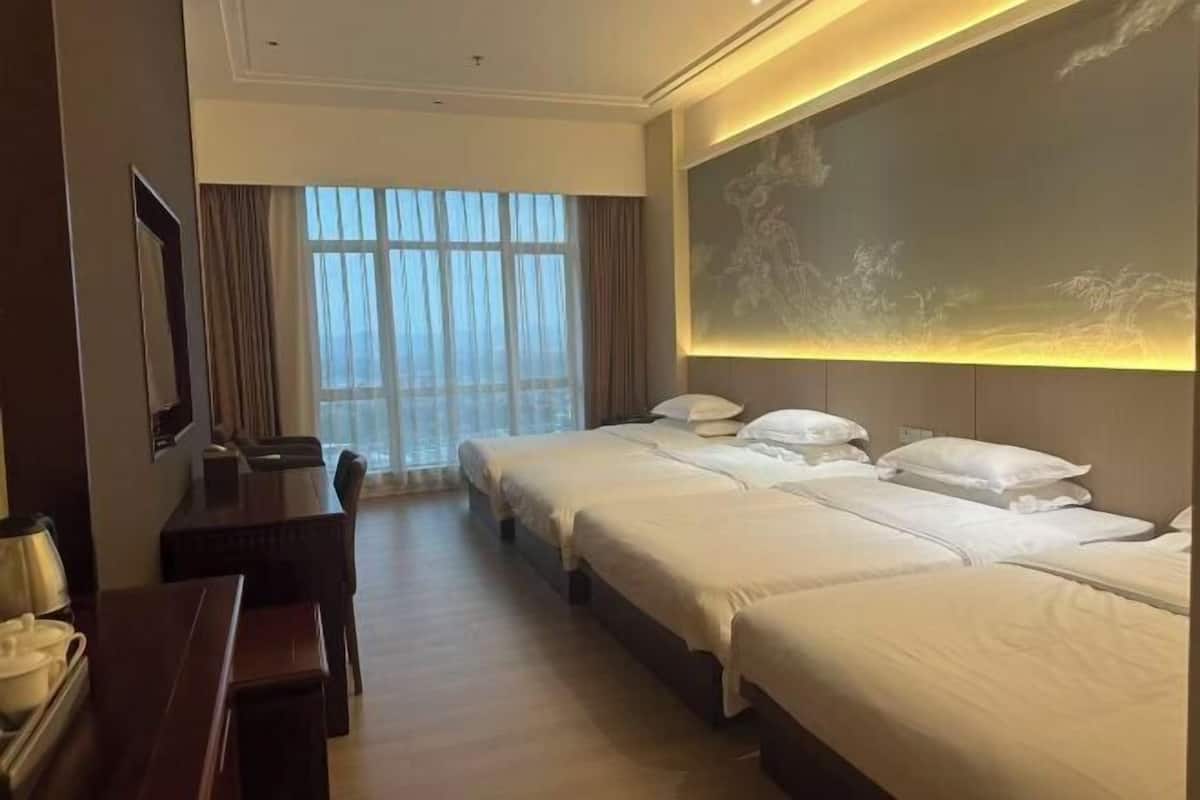 A hotel room with two beds, a desk, and a large window.