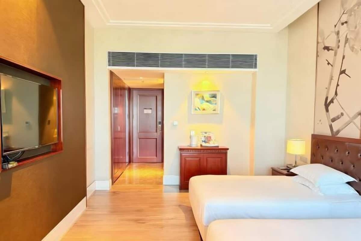 A hotel room with a bed, a nightstand, a TV mounted on the wall, and a door leading to another room.